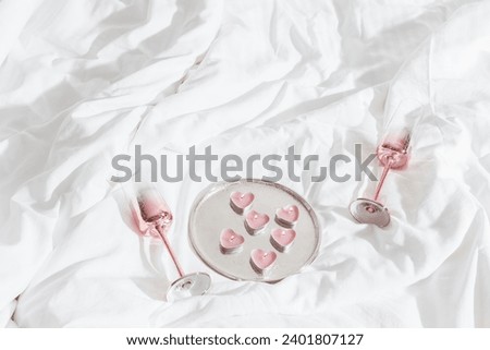 Pink shining champagne glasses and burning candles as hearts on bed cloth. Lifestyle aesthetic photo, star filter effect. Valentine's Day, love concept, romance meeting. Sparkling wine in wineglasses.