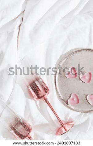 Pink shining champagne glasses and burning candles as hearts on bed cloth. Lifestyle aesthetic photo, star filter effect. Valentine's Day, love concept, romance meeting. Sparkling wine in wineglasses.