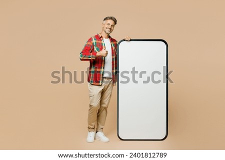 Full body adult man he wearing red shirt white t-shirt casual clothes big huge blank screen mobile cell phone smartphone with area show thumb up isolated on plain pastel light beige color background
