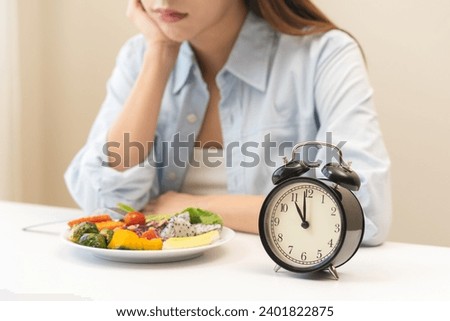 Intermittent fasting with clock, close up young woman, girl diet, waiting time to eat ketogenic low carb, green vegetable salad on plate. Eat food healthy first meal on brunch, lunch on table at home.