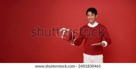 Young man of Asian ethnicity wear red sweater hold red present box with gift ribbon bow isolated on red copy space background. birthday, valentines day, new year concept. Royalty-Free Stock Photo #2401830461