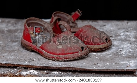 A pair of old, red sandals covered in dust are abandoned on a grey surface. Royalty-Free Stock Photo #2401833139