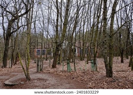 A structure with a blue blue windows surrounded by trees. The facade of an abandoned kindergarten in the Chernobyl radioactive zone. Autumn foliage on the ground. Trees in front of an old house. Royalty-Free Stock Photo #2401833229