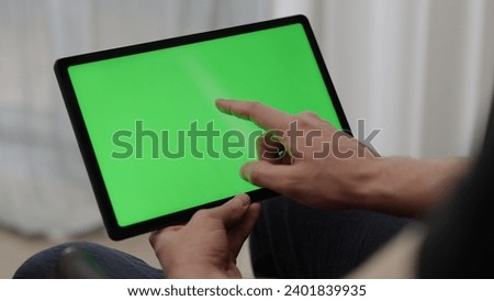 Man sitting indoors on a chair with tablet pc with green screen