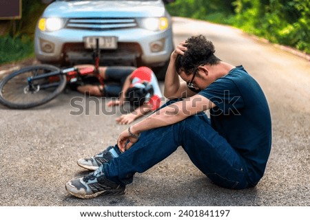 Young Asian man sitting on the road worrying after driving car crashes into a cyclist falls and injures, Cyclist in Need of Urgent Aid, Unexpected Roadside Encounter, Outdoor Mishaps Car Crash. Royalty-Free Stock Photo #2401841197