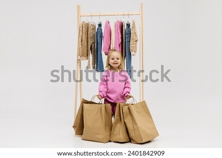 A child, a little girl, stands near the closet, chooses clothes against a light background. Dressing room with clothes on hangers. Wardrobe of children's and stylish clothes. Montessori wardrobe. Royalty-Free Stock Photo #2401842909