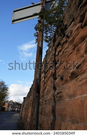 Rusty sign post pole with sign on top next to stone brick wall