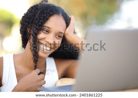 Happy black woman playing with hair watching media on laptop outdoors