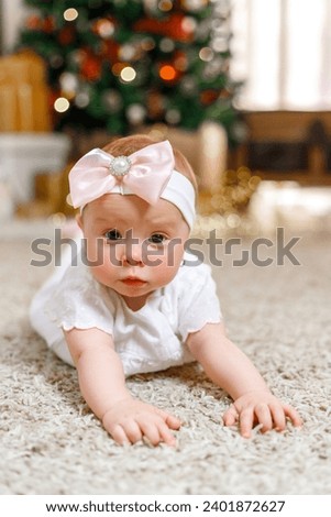 Cute little newborn girl on a soft carpet near the Christmas tree, happy childhood. Merry Christmas and Happy Holidays!