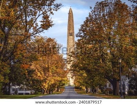 Bennington Battle Monument looking north on a clear Autumn day with Fall foliage draping over the street. Royalty-Free Stock Photo #2401879517
