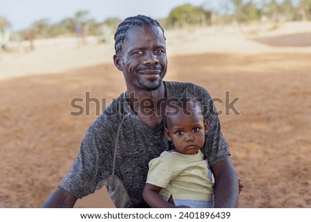 village young african father with child, standing in the yard in a sunny day , man with a dreadlocks hairstyle Royalty-Free Stock Photo #2401896439