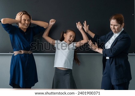 The female teacher screams at the schoolgirl and her mother standing at the blackboard.  Royalty-Free Stock Photo #2401900371