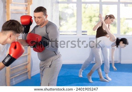 Sportive middle-aged man training boxing in pair with his partner during sports classes