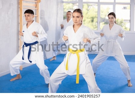 Diligent young woman attendee of karate classes practicing kata standing in row with others in sports hall