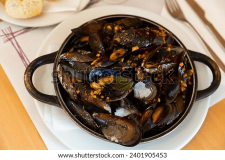 Popular appetizing dish of Spanish cuisine of grilled mussels with minced meat, served in a frying pan