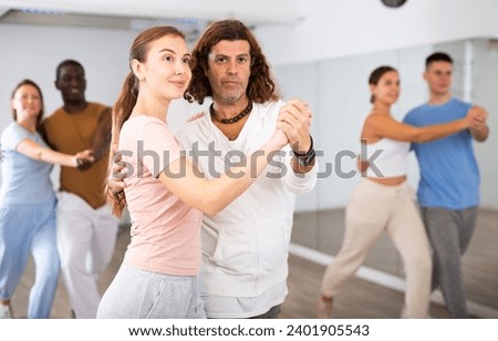 Smiling multiracial men and women enjoying partner dance while training together in modern studio Royalty-Free Stock Photo #2401905543