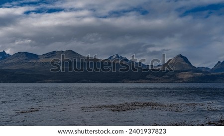 A beautiful snow-capped mountain range of the Andes against the background of the sky, clouds and the Beagle Channel. Ripples on the water. Argentina. Tierra del Fuego Archipelago.