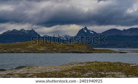 A picturesque mountain range of the Andes against a cloudy sky. The islets in the Beagle Channel are covered with sparse stunted vegetation. Argentina. Patagonia. Tierra del Fuego Archipelago