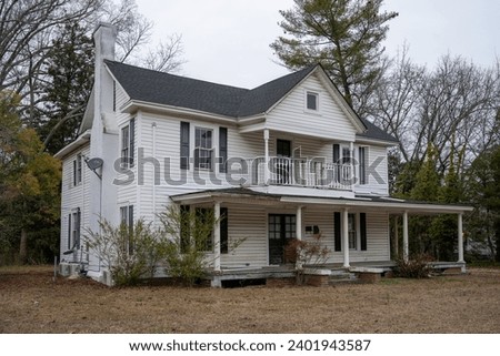 An old white plantation-style home in Clover, South Carolina, exudes timeless southern charm. With its iconic white columns, expansive front porch, and surrounded by majestic oak trees. Royalty-Free Stock Photo #2401943587
