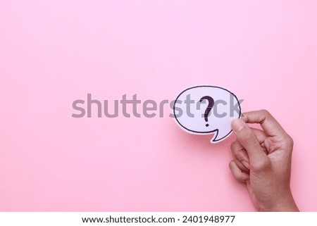 Hand holding paper with question marks symbol on pink background