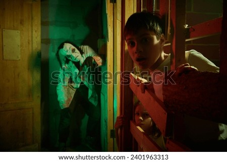 Two teenagers - a boy and a girl - have fallen into the trap of a maniac and are looking in fear from behind the bars of the cage. Horror film for teenagers. Halloween scary quest. Royalty-Free Stock Photo #2401963313