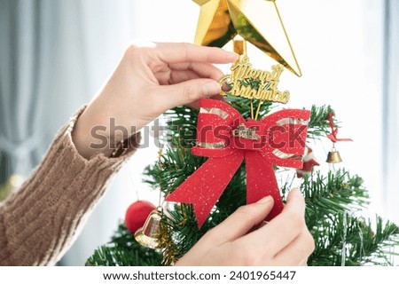Woman hands hanging a red bow on decorated Christmas tree during Christmas festival and New Year celebration.