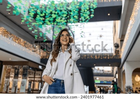 Copy space shot of a young woman smiling while talking on cell phone at the shopping mall. She is doing her Christmas shopping.