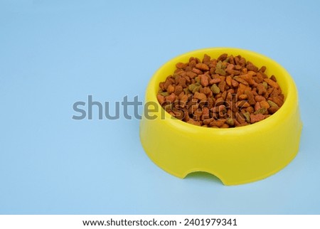 Dry cat food in yellow bowl on blue background, space for text.