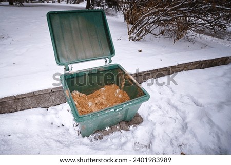 Sand box with sand for improve traction on snowy and icy sidewalk, road maintenance in winter season. Plastic grit container, spread sand to prevent slipping. Grit bin Royalty-Free Stock Photo #2401983989