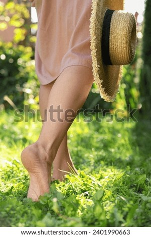 Woman with straw hat walking barefoot on green grass outdoors, closeup Royalty-Free Stock Photo #2401990663