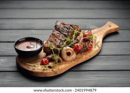 hot grilled spare ribs from a summer BBQ served with a grilled vegetables and sauce on an old vintage wooden cutting board. Copy space Royalty-Free Stock Photo #2401994879