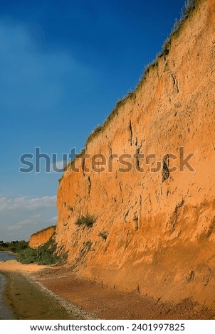 Clay cliffs on Dniper-Bug estuary. Change in lightness or color tone of object depending on environment is called simultaneous color contrast - blue of sky is enhanced by precipice yellow-ochre color Royalty-Free Stock Photo #2401997825