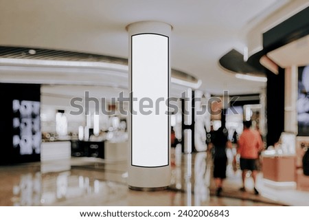 Advertising digital screen on pillar in shopping mall. Vertical OOH out of home poster display in retail environment. Out of focus bokeh effect in background. Royalty-Free Stock Photo #2402006843