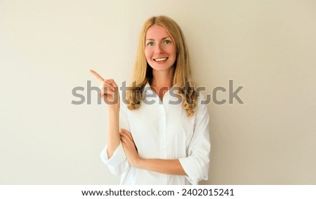 Portrait of happy smiling young woman pointing her finger to the side and looking at camera on studio background, blank copy space for advertising text