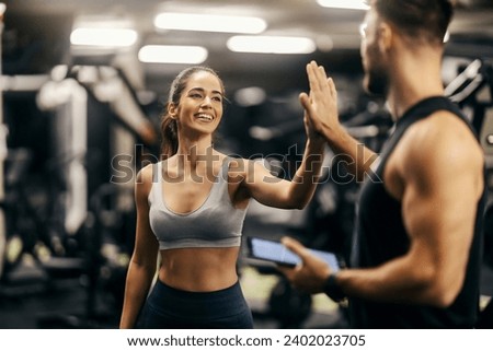Portrait of a fit happy sportswoman giving high five to her coach in a gym. Gym workout. Fitness trainer. Royalty-Free Stock Photo #2402023705