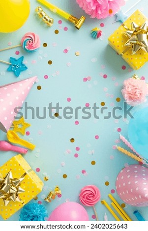 Exciting birthday concept composition. Overhead vertical image of festively decorated table with gifts, birthday hats, balloons, confetti, and more against soft blue backdrop. Ideal for text or advert