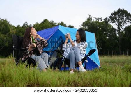 Asian women travelers sit enjoy drinking beer and take pictures near the camping tent in the evening time in a romantic natural atmosphere.