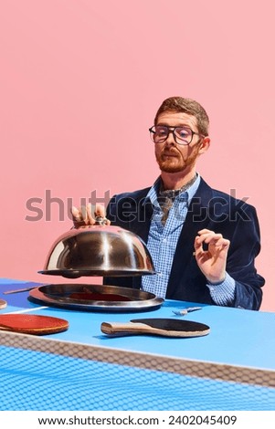 Cooking. Creative photography with man in elegant clothes opening dish with table tennis racket over pink background. Concept of sport, leisure, hobby, creativity, fun and joy. Pop art