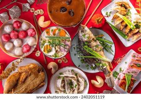 Traditional Chinese lunar New Year dinner table, party invitation, menu background with pork, fried fish, chicken, rice balls, dumplings, fortune cookie, nian gao cake, noodles, chinese decorations Royalty-Free Stock Photo #2402051119