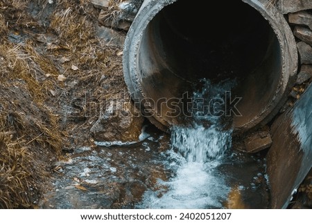 A sewage pipe drains toxic wastewater into a river, causing environmental pollution and ecological damage. Royalty-Free Stock Photo #2402051207