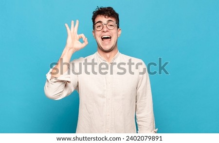 young man feeling successful and satisfied, smiling with mouth wide open, making okay sign with hand