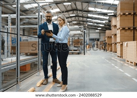 Female engineer and male production manager standing in modern industrial factory, talking about production. Manufacturing facility with robotics and automation.