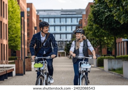 Spouses commuting through the city, riding bike on street. Middle-aged city commuters traveling from work by bike after a long workday. Royalty-Free Stock Photo #2402088543