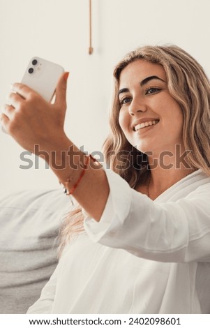 Selfie picture of happy beautiful young woman looking at camera with toothy smile. Pretty girl holding gadget with webcam, making video call, self home portrait. Communication concept