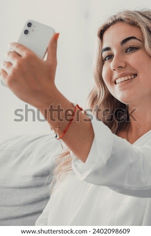 Selfie picture of happy beautiful young woman looking at camera with toothy smile. Pretty girl holding gadget with webcam, making video call, self home portrait. Communication concept