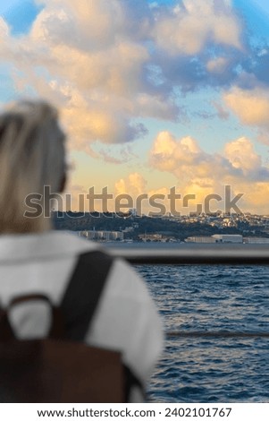 Young female traveler in a white shirt and with a craft backpack enjoys a magnificent view of the Bosphorus and the European part in Istanbul, selective focus. Vertical photo