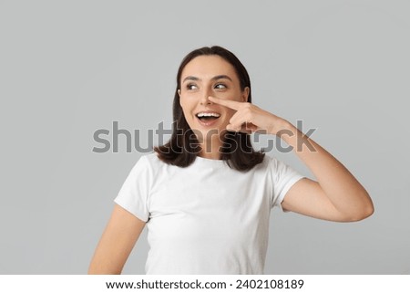Young woman touching her nose on light background Royalty-Free Stock Photo #2402108189