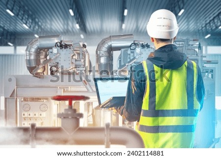 Man factory employee. Guy works at enterprise. Technologist is standing in workshop. Factory contractor with laptop. Engineer in hangar with industrial equipment. Man technologist back to camera Royalty-Free Stock Photo #2402114881