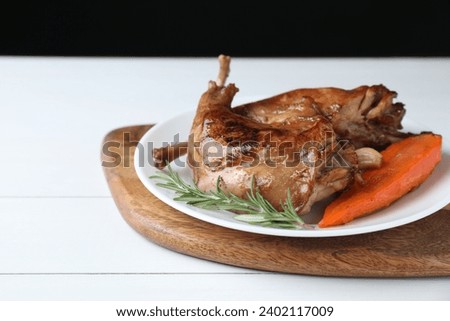 Tasty cooked rabbit meat with rosemary, garlic and carrot on white wooden table, closeup. Space for text