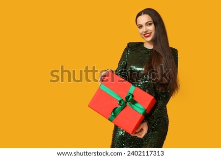 Beautiful young woman with Christmas gift on yellow background